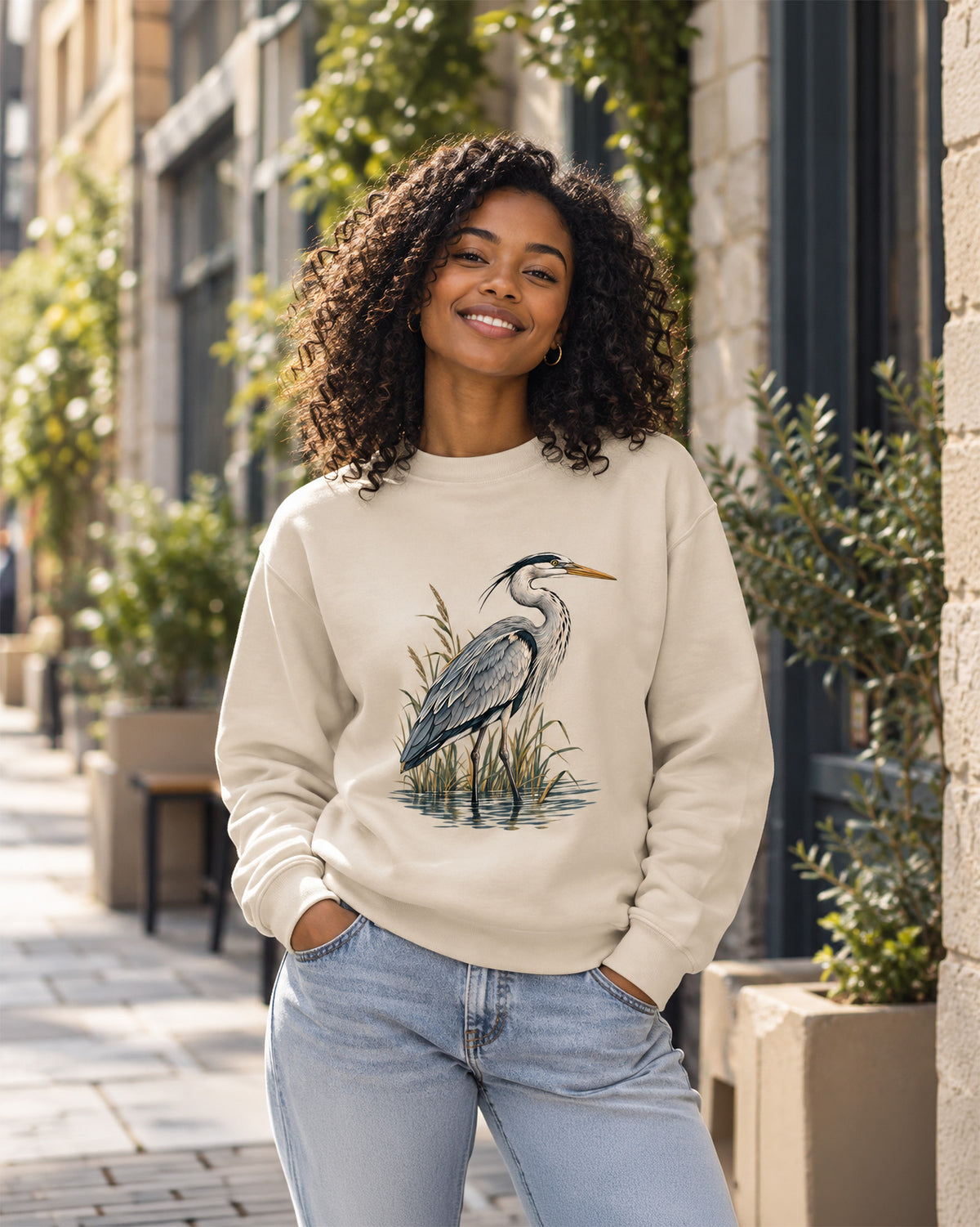 Lifestyle photo of woman wearing Desert Dust organic cotton sweatshirt with Grey Heron illustration designed by Gaia's Harmony. Color: desert dust