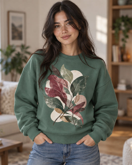 Woman wearing a relaxed green sweatshirt featuring an abstract botanical leaf design by Gaia's Harmony in burgundy, sage, pine and neutral tones